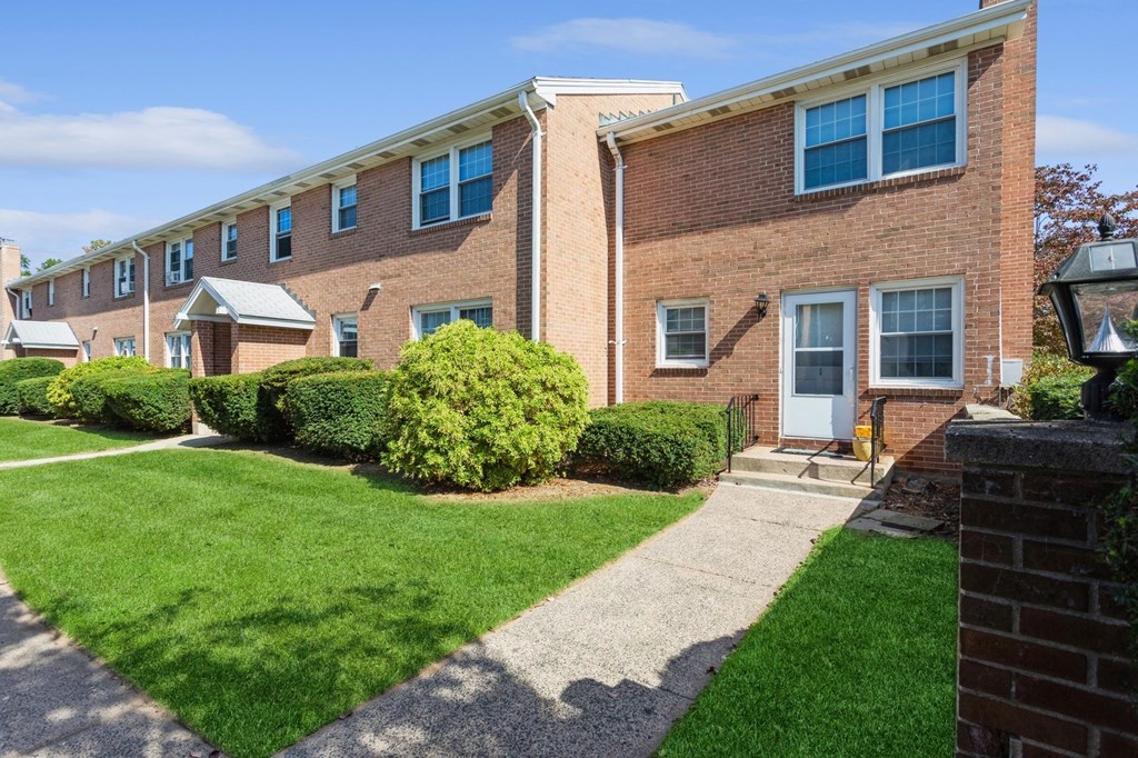 the front of a brick apartment building with a sidewalk and grass