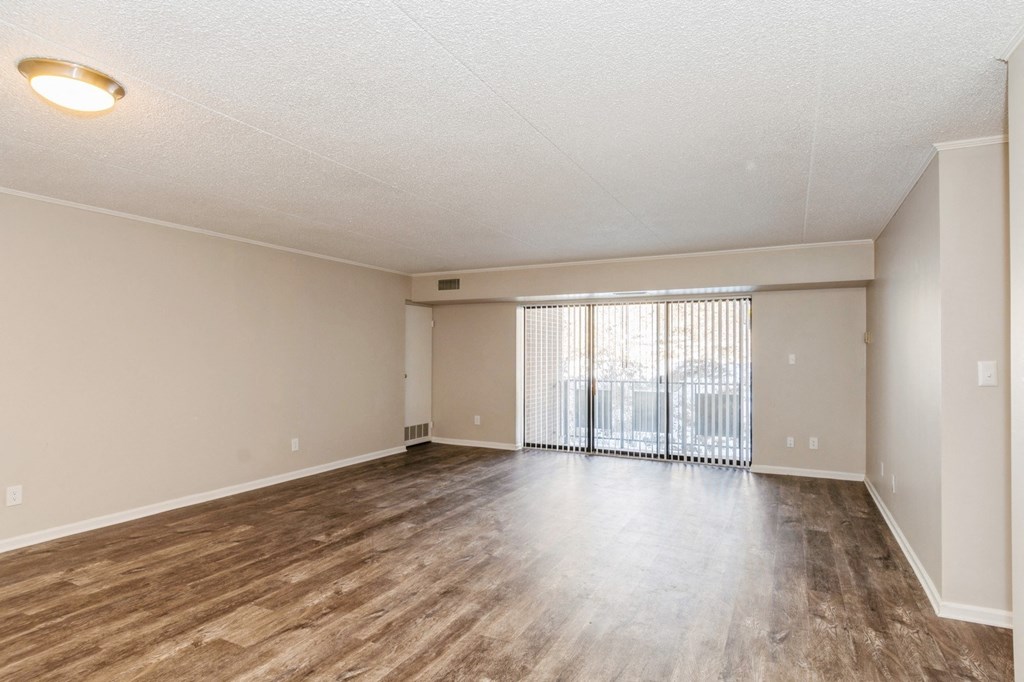 A spacious room with wooden flooring and a sliding glass door.