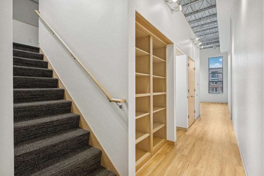 A staircase with a wooden handrail and steps covered in a textured carpet leads up to a doorway.