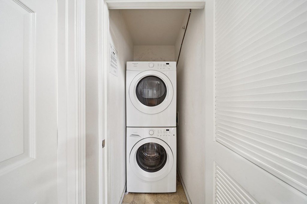 A white washing machine and dryer in a small, white-walled laundry room.