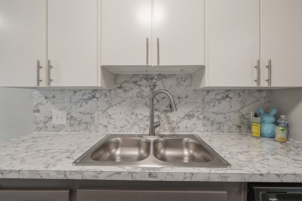 a kitchen sink with marble counter top and white cabinets
