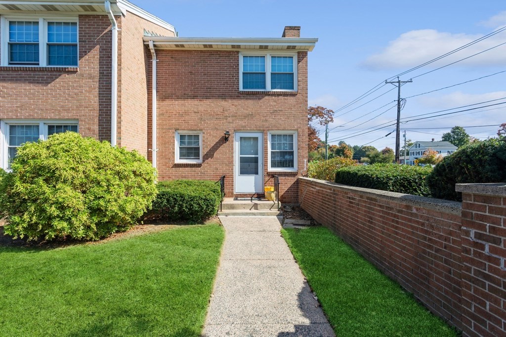 the front of a brick house with a sidewalk and grass