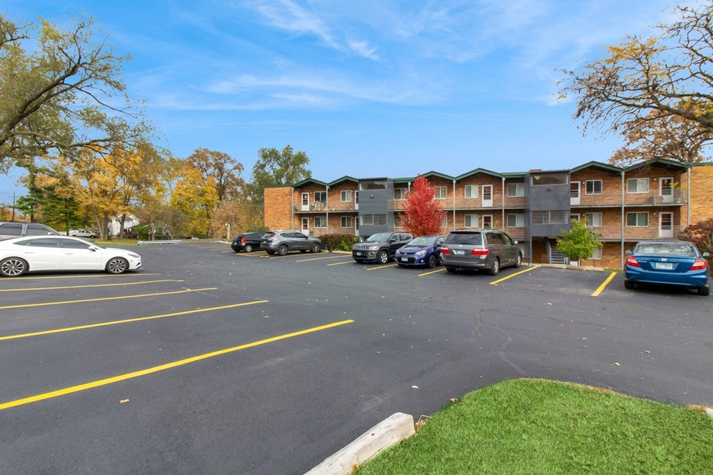 an empty parking lot with cars in front of an apartment building at River Oaks, North Aurora, IL