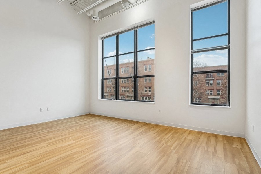 A room with wooden floors and two windows showing a view of a building.