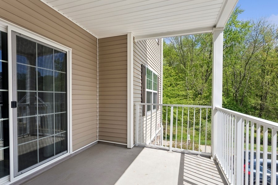A screened porch with a white railing and a view of trees.