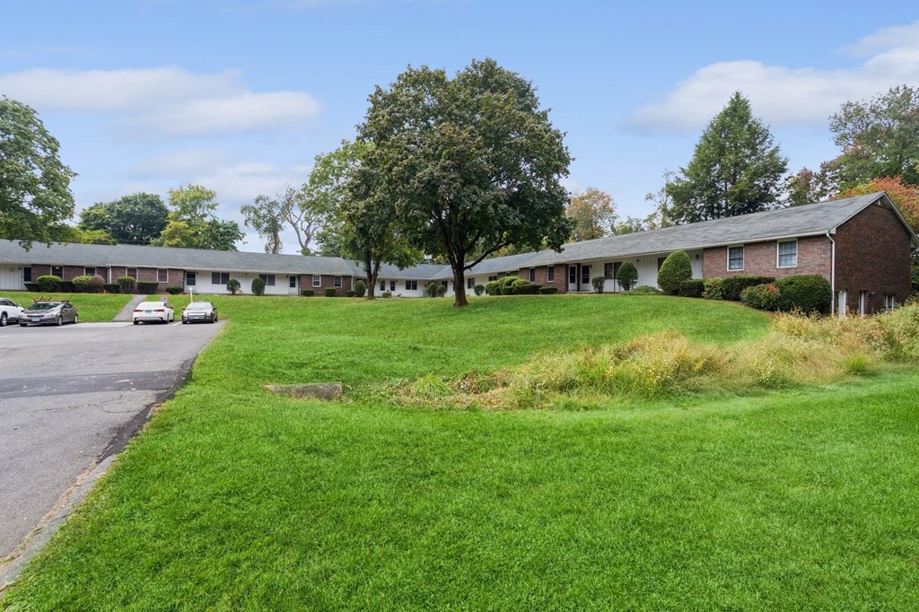 the front of a building with a green lawn and a parking lot