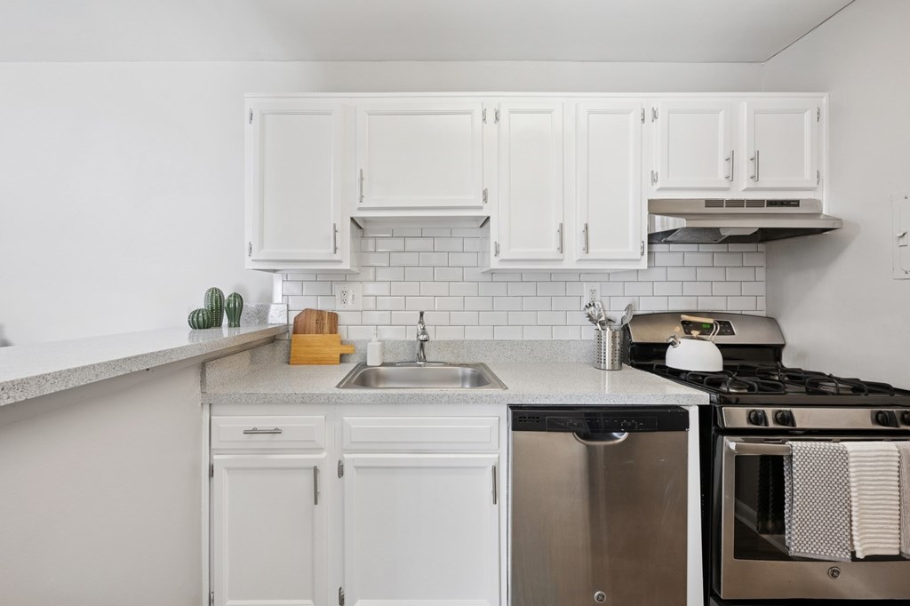 A white kitchen with a stove, sink, and cabinets.