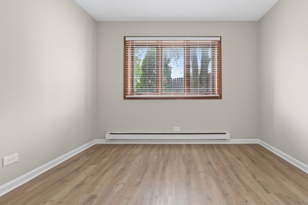 A room with a window and a radiator on a wooden floor.