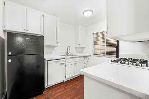 A black refrigerator sits in a kitchen with white cabinets and a white countertop.