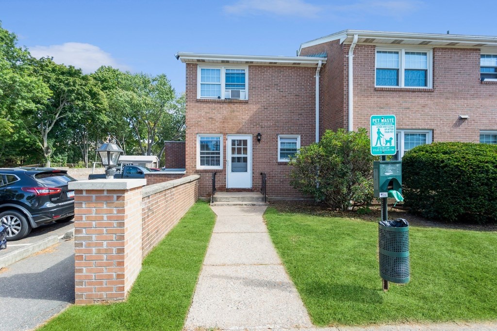 the front of a brick apartment with a sidewalk and a doggy trash station