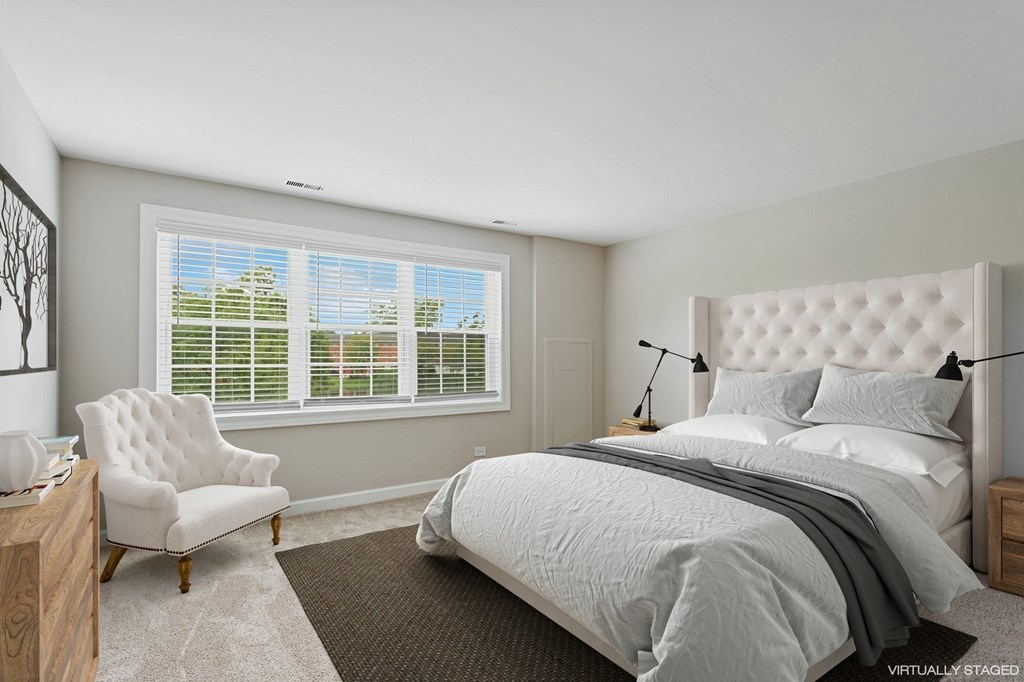 A bedroom with a large bed, a chair, and a window with blinds.