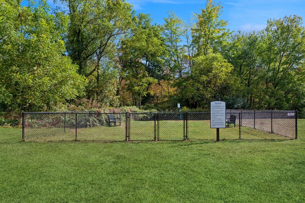 a dog park with a fence and a sign in the grass with the rules at Arbor Commons