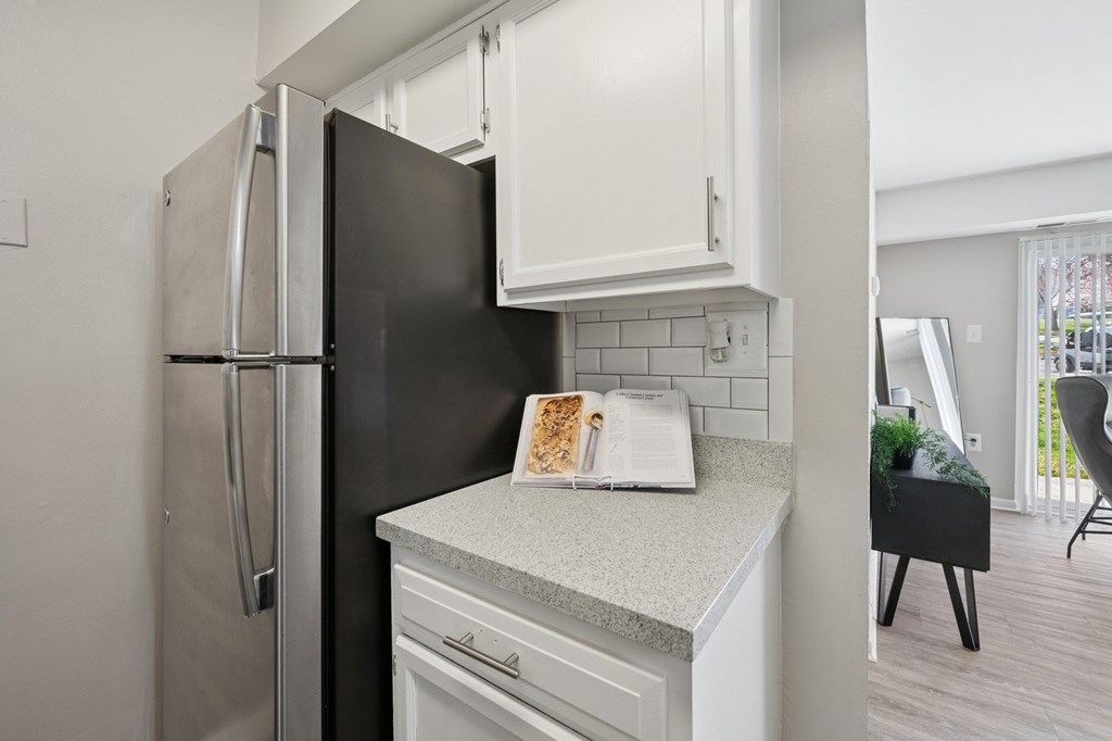 A black refrigerator is in a kitchen with white cabinets and a countertop.