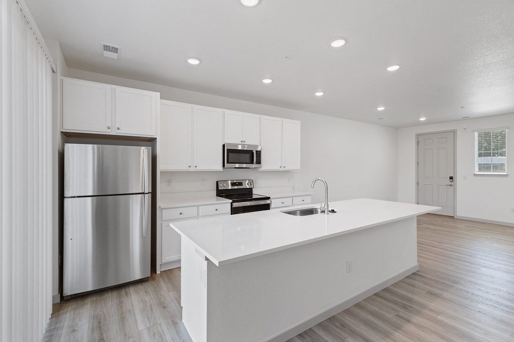 a white kitchen with a large island and stainless steel refrigerator