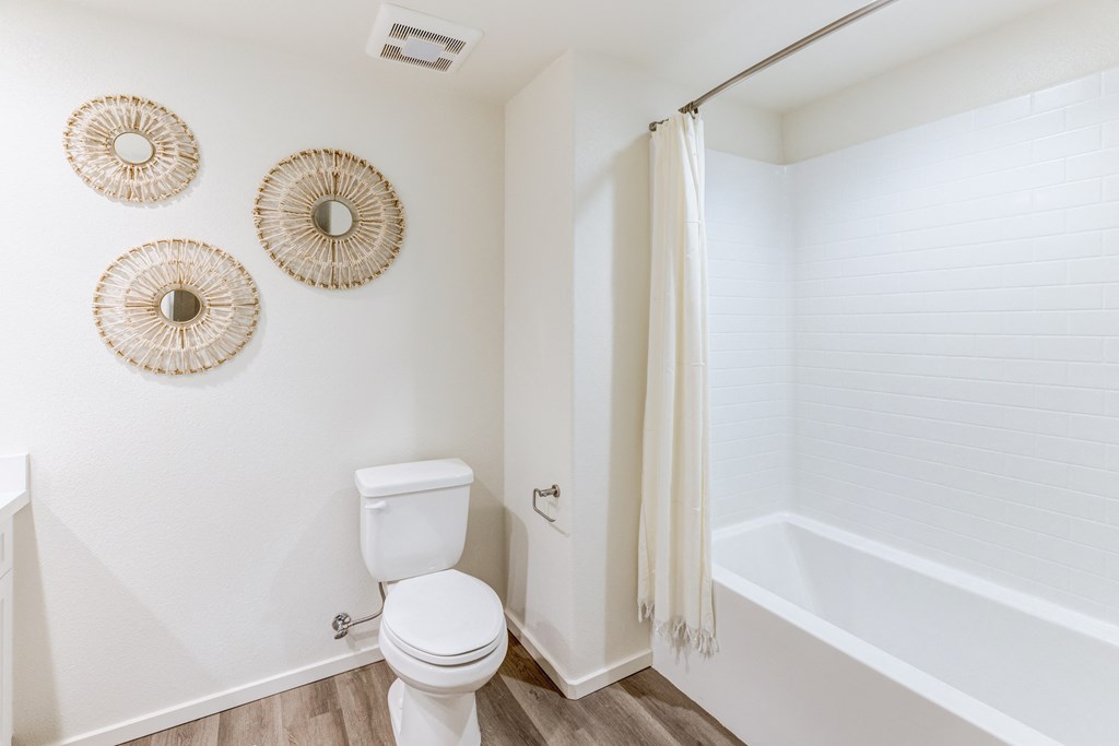 A white toilet sits in a bathroom with three wall hangings.