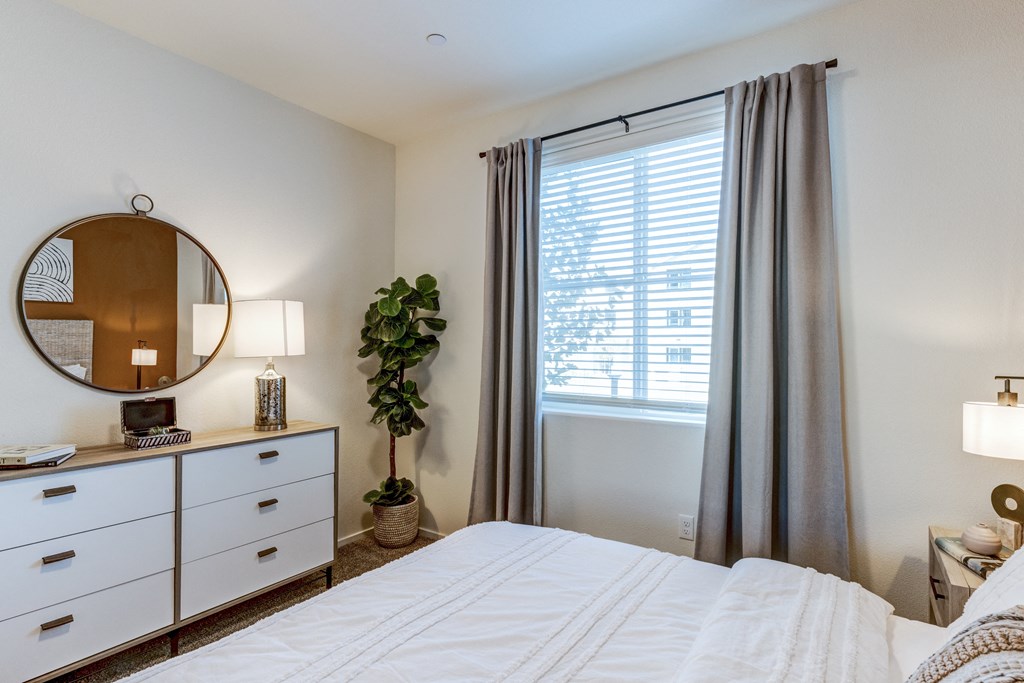 A bedroom with a large bed, a mirror, and a potted plant.