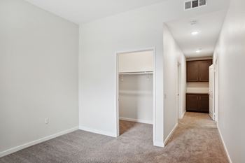 A sparsely furnished bedroom with a carpeted floor and a closet with a sliding door.