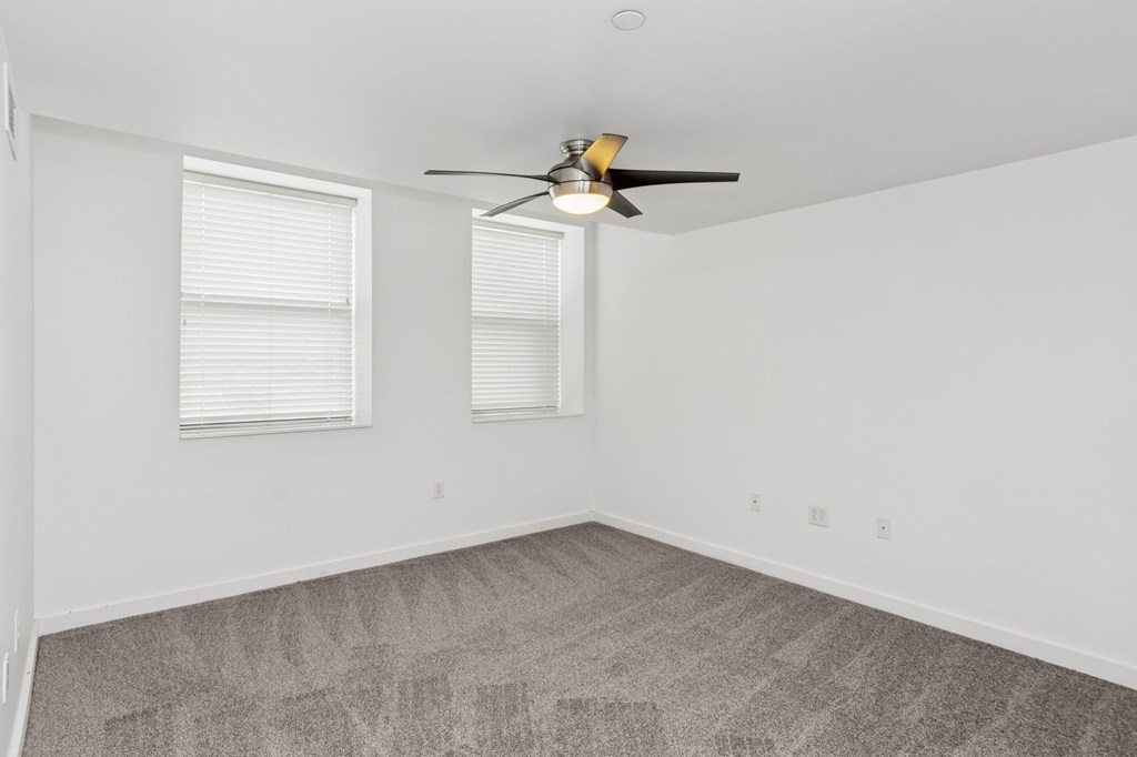 A room with a ceiling fan and two windows.