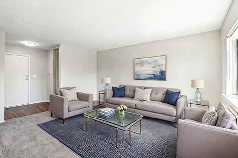 A living room with a grey couch, a grey armchair, a glass coffee table and a painting on the wall.
