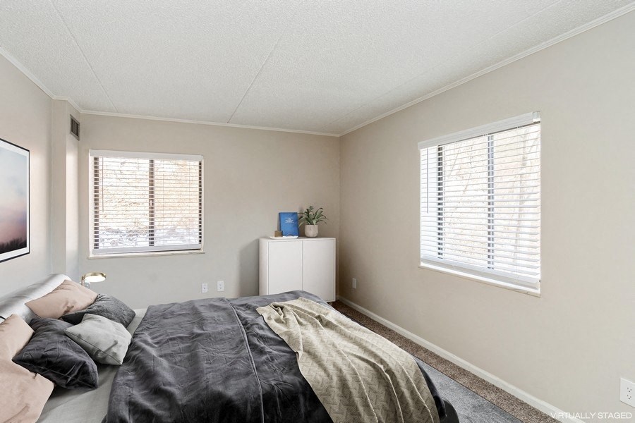 A bedroom with a bed, a nightstand, and a window with blinds.