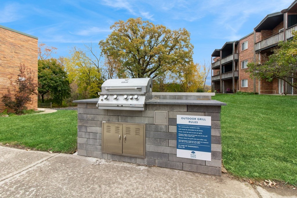a barbecue grill sits on a brick structure in the middle of a grass field at River Oaks, North Aurora, IL