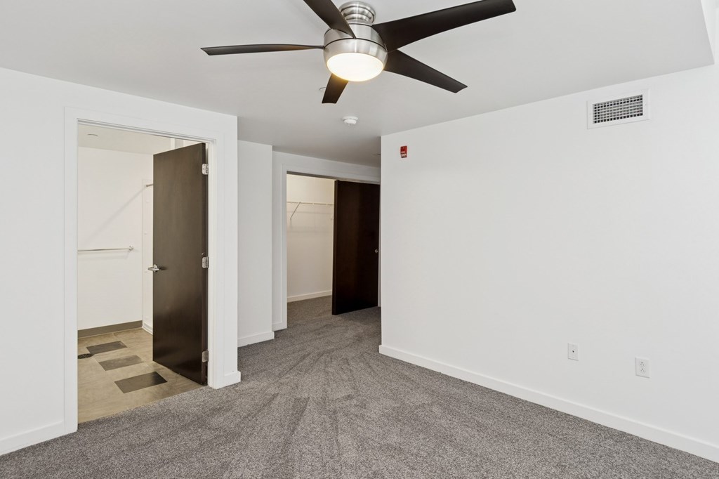 A room with a ceiling fan and carpeted floor.