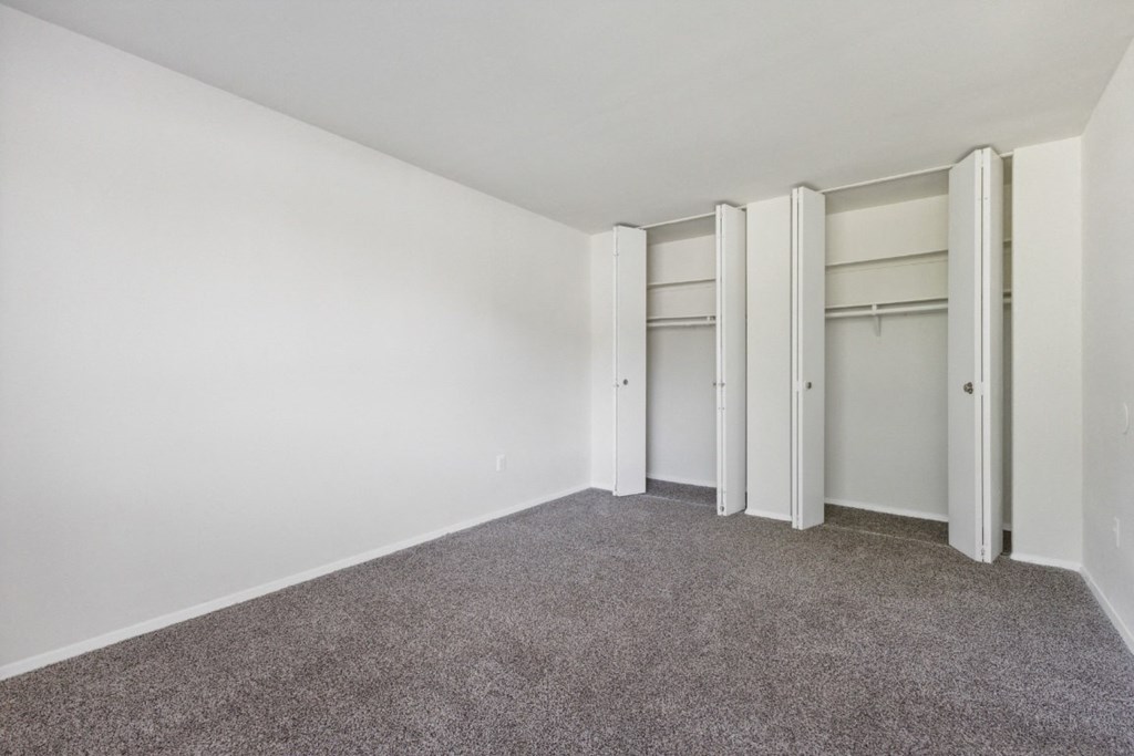 an empty room with white walls and carpet and closet doors at Briarwood Apartments, Dumfries, VA