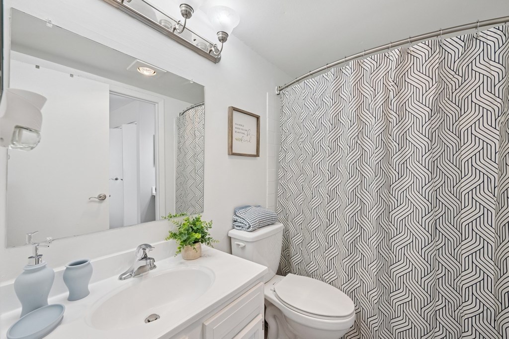 A bathroom with a white sink, toilet, and a grey and white shower curtain.