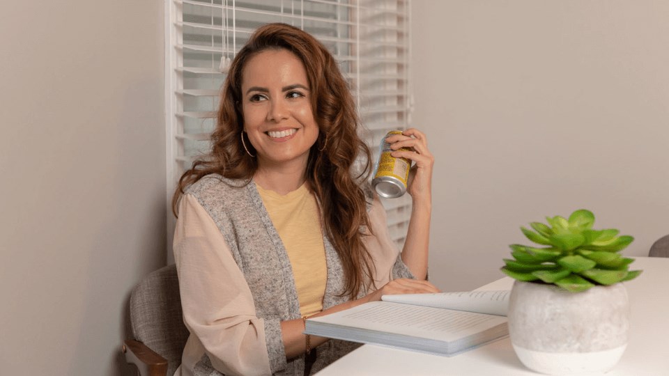 a woman sitting at a table with a book and a can of beer  at The View Apartments St Charles, St Charles, Illinois