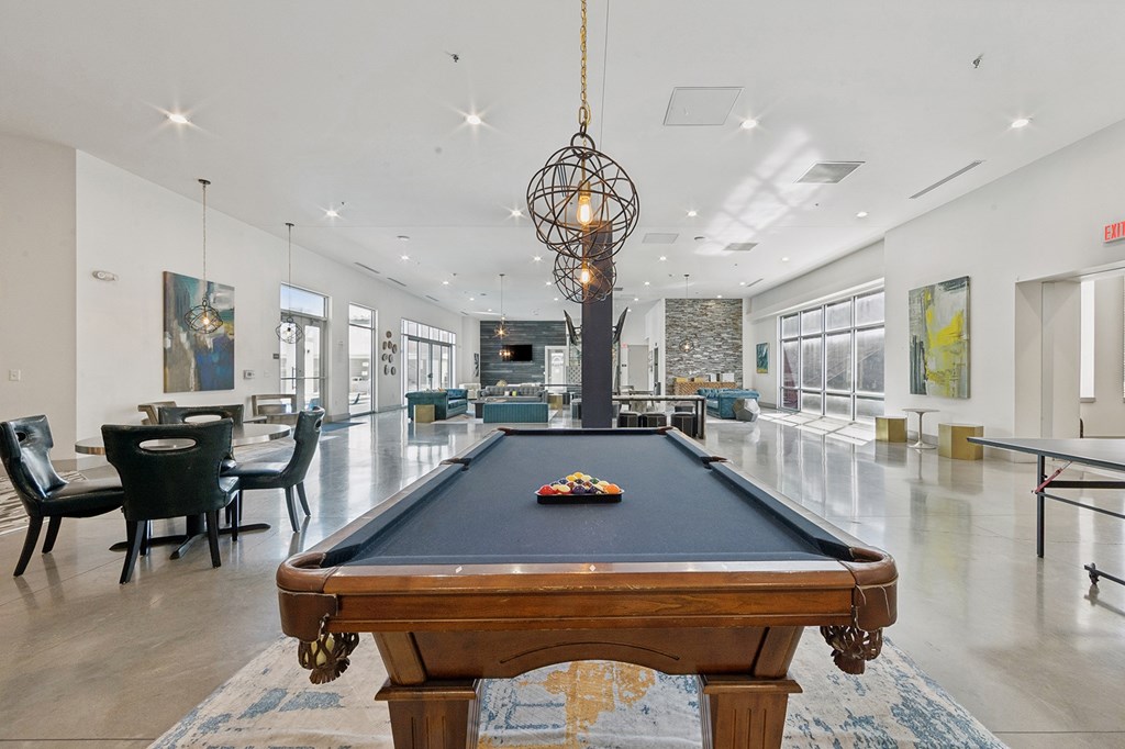 A pool table is in the middle of a room with a black chair and a chandelier.