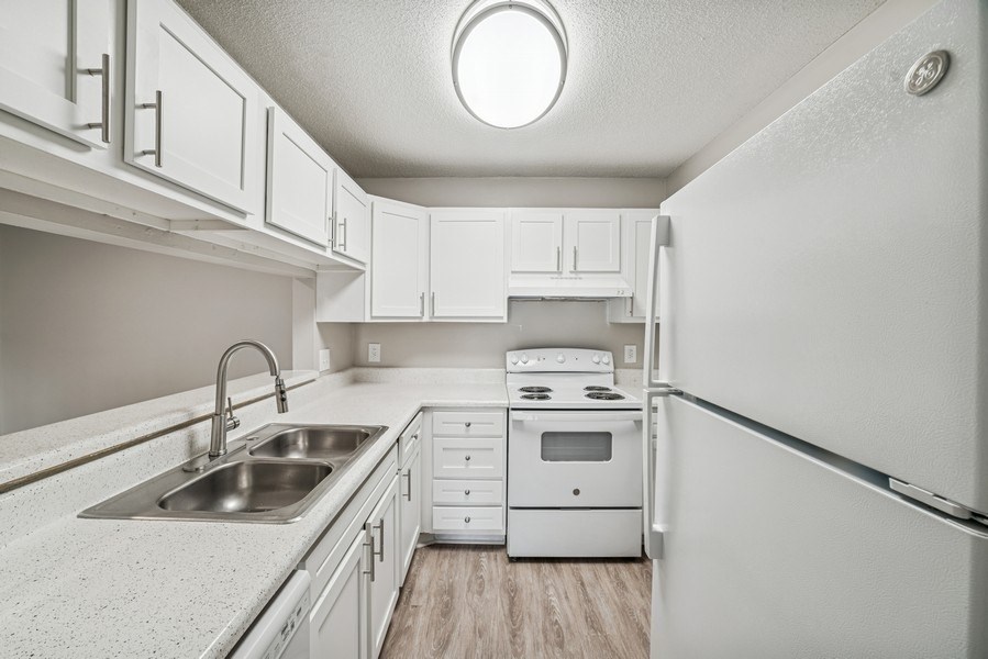 A white kitchen with a sink, stove, and refrigerator.