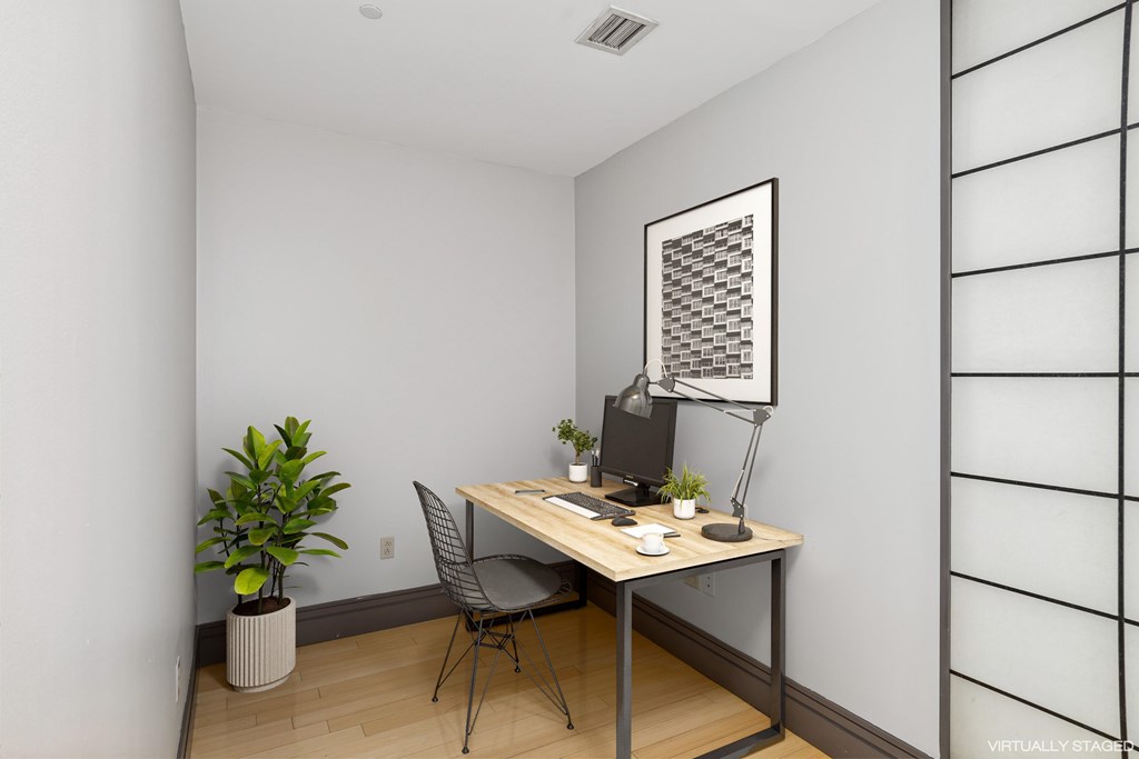 A room with a desk, chair, and a potted plant.