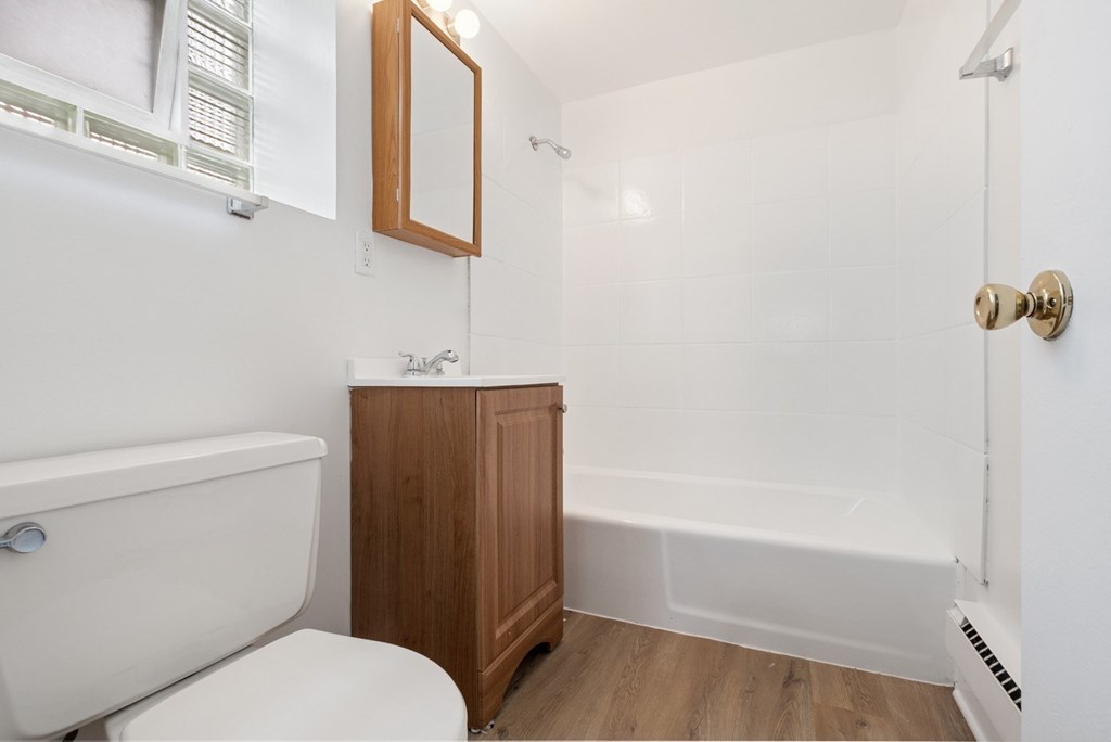 A white bathroom with a wooden cabinet and a white tub.