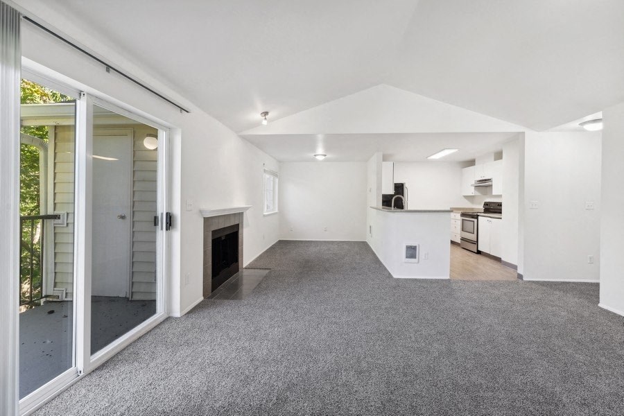 an empty living room with a fireplace and a kitchen