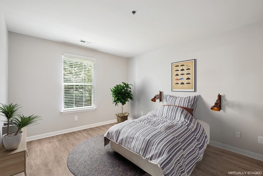 A bedroom with a bed, a plant, and a picture on the wall.