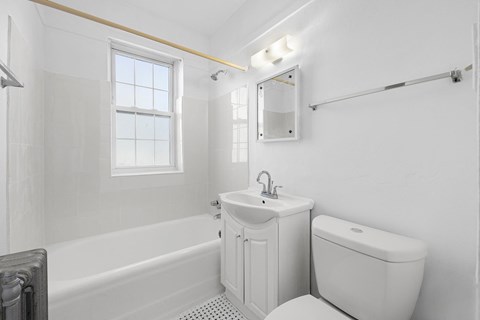 A white bathroom with a tub, toilet, sink, and mirror at Pleasant Oak Apartments, Oak Park, IL, 60302
