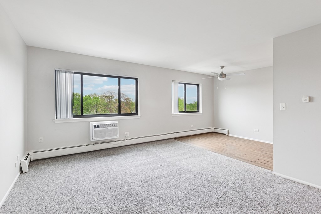 A spacious room with a grey carpet and kitchen in the background