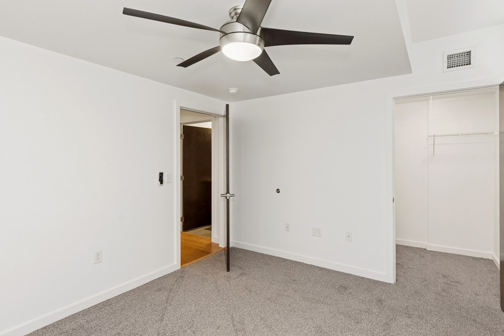 A room with a ceiling fan and a door leading to another room.