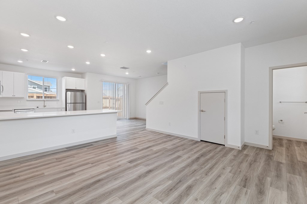 a renovated living room and kitchen with white walls and wood flooring