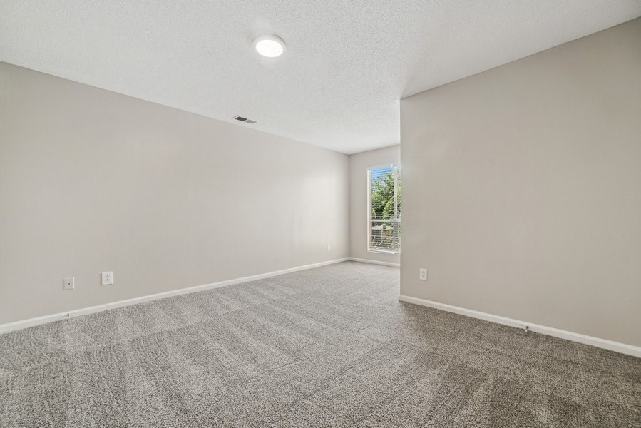 A spacious living room with a carpeted floor and a window.