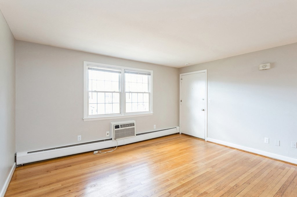 an empty room with wood floors, a white wall, and window