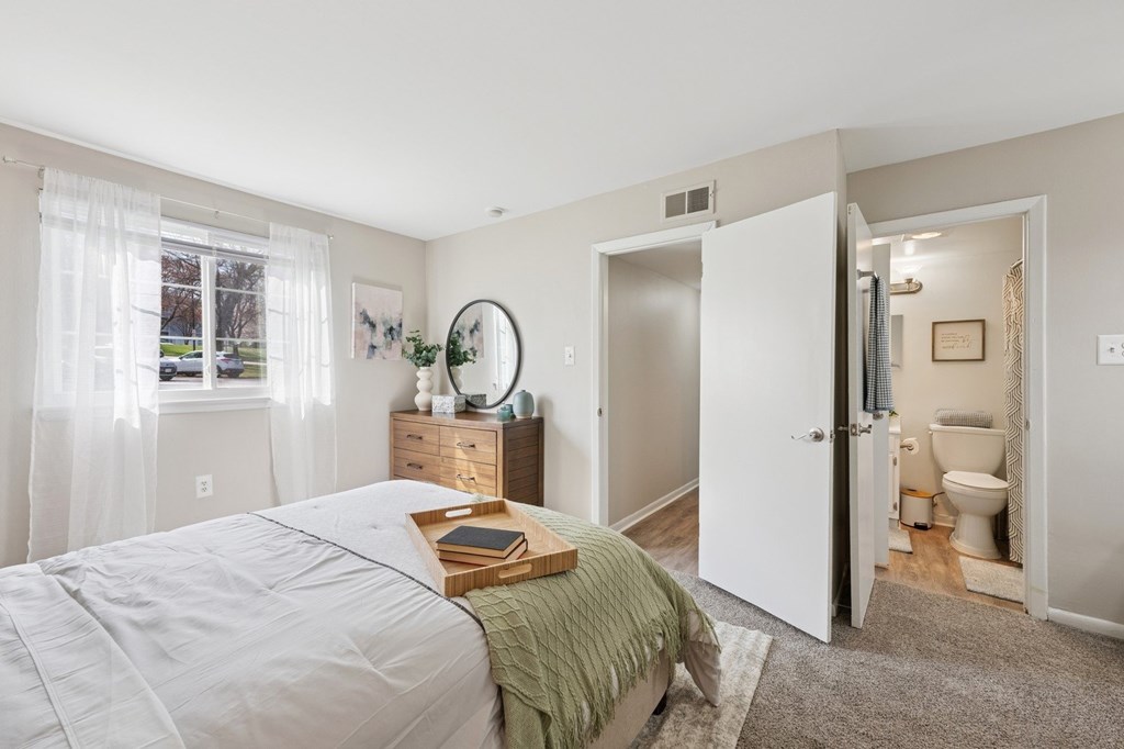 A bedroom with a bed, nightstand, and a bathroom visible through the open door.