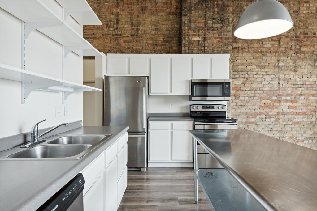 a kitchen with stainless steel countertops and a brick wallat Gaar Scott Historic Lofts, Minneapolis