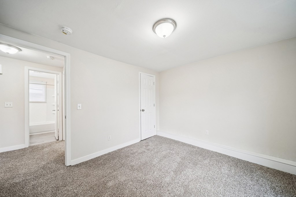 A room with a carpeted floor and a smoke detector on the ceiling.