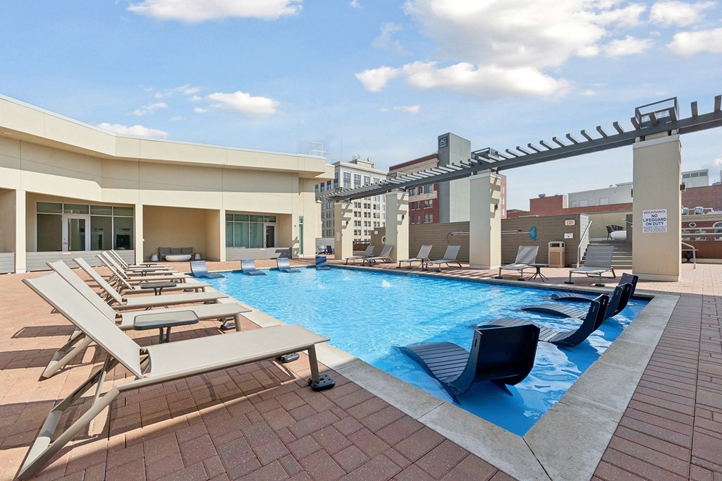 Rooftop pool with sun loungers and a building in the background.