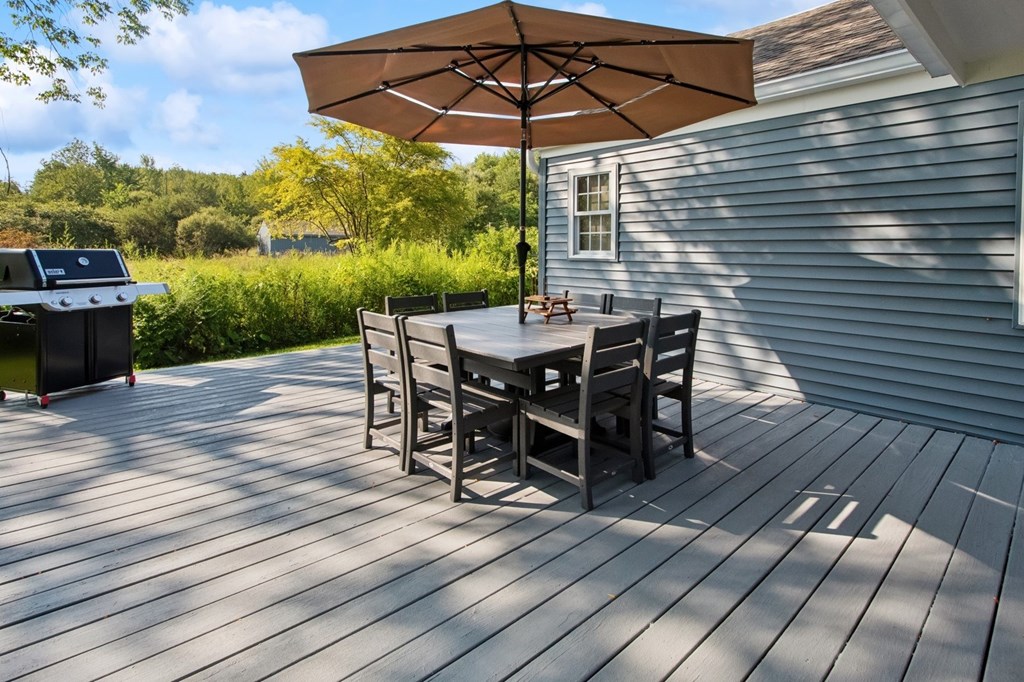 A table with chairs and an umbrella on a wooden deck.