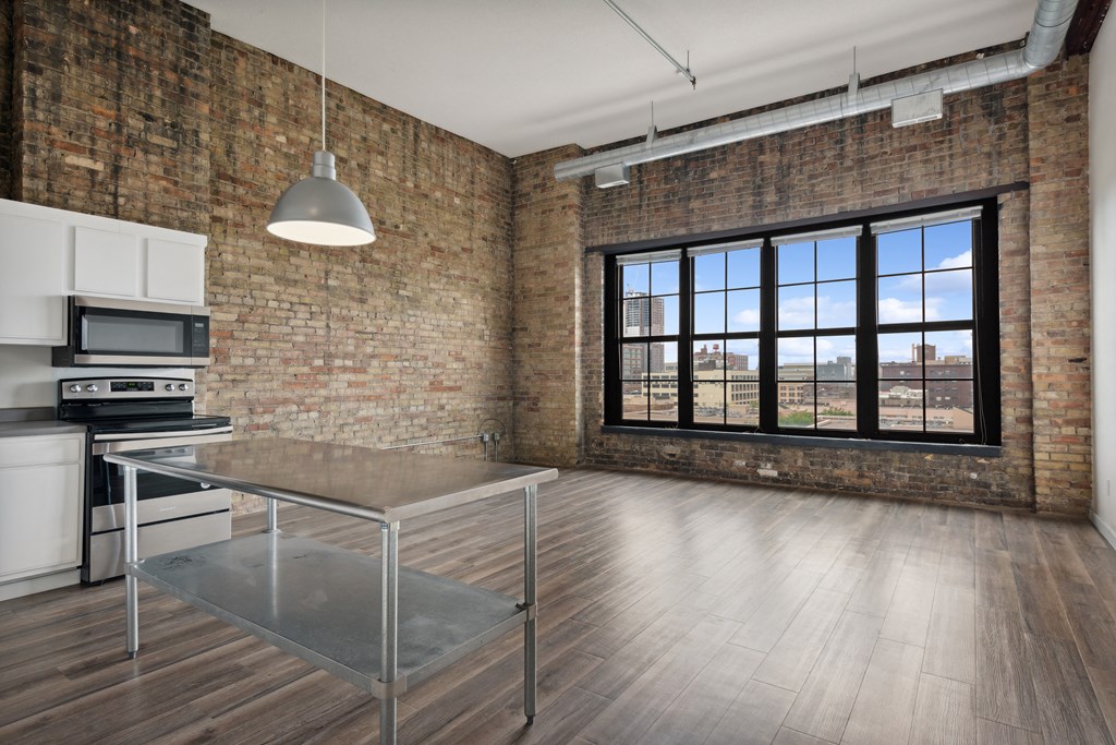 an open kitchen and dining area in an apartment with brick walls and a large windowat Gaar Scott Historic Lofts, Minnesota, 55401
