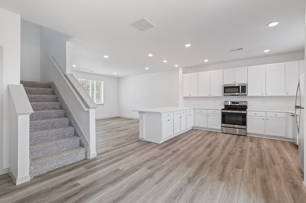 an open kitchen and living room with white cabinets and a staircase