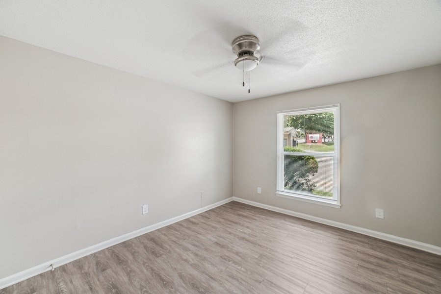 A room with a ceiling fan and a window showing a view of a house and trees.