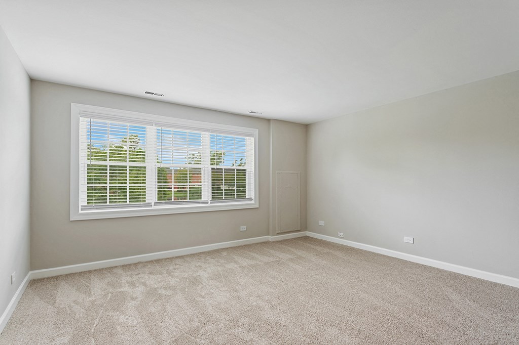 a bedroom with a large window and beige carpet at The Hinsdale, Illinois